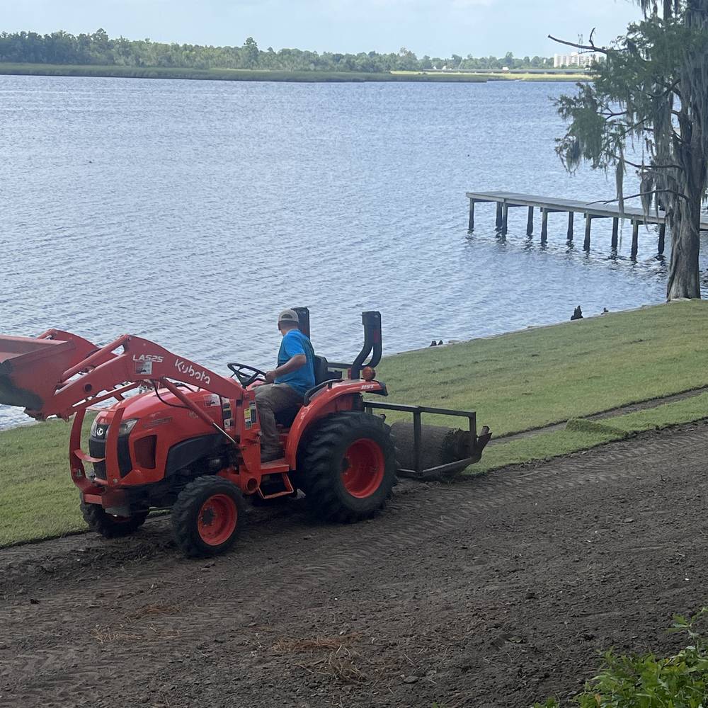 Tractor laying sod on a waterfront lawn with crew member raking
